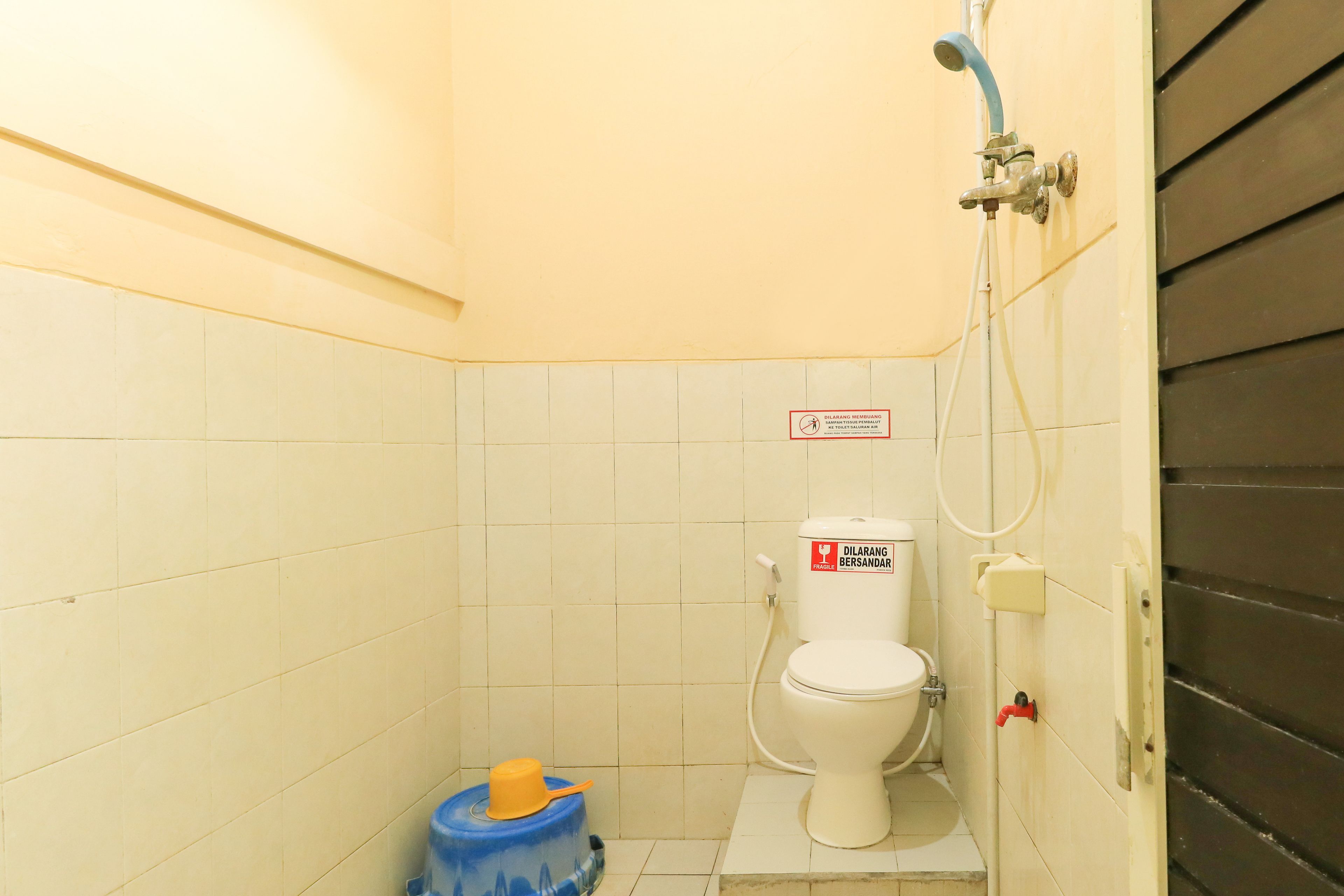 A small, basic bathroom with a toilet, a shower, and a blue water dispenser.