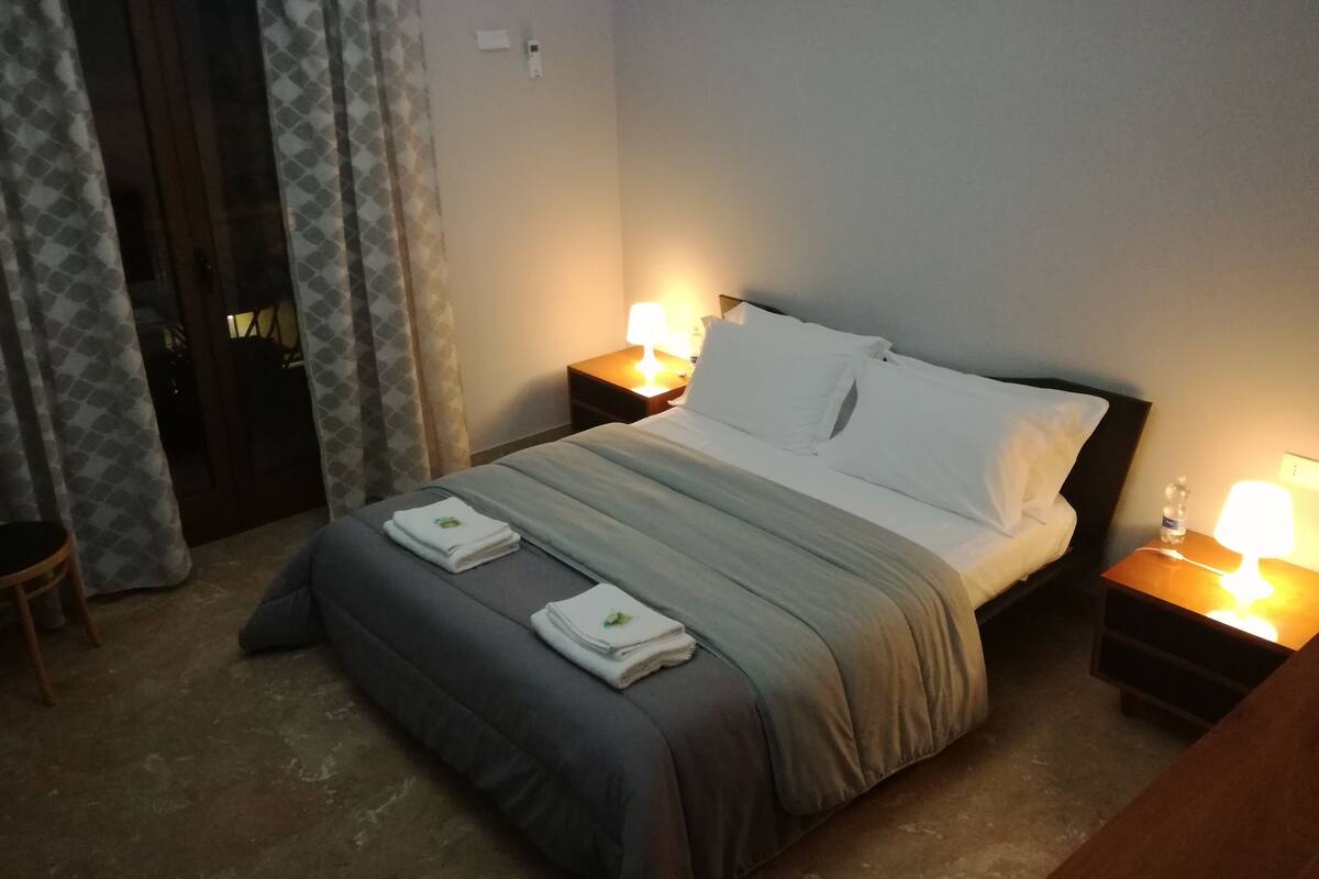 A hotel room with a bed, two bedside tables, a chair, and a curtain.