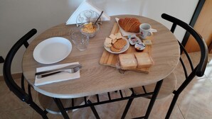 A round wooden table with a white plate, a glass, a napkin, a knife, a bowl of chips, a croissant, a plate of cheese, a cup of coffee, and a jar of jam. - Home La Kore (Agrigento)