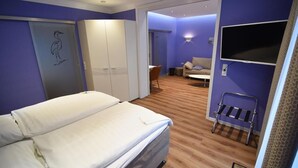 A hotel room with a bed, a wardrobe, a TV, and a seating area with a sofa and a chair. - Haus am Meer (Wunstorf)