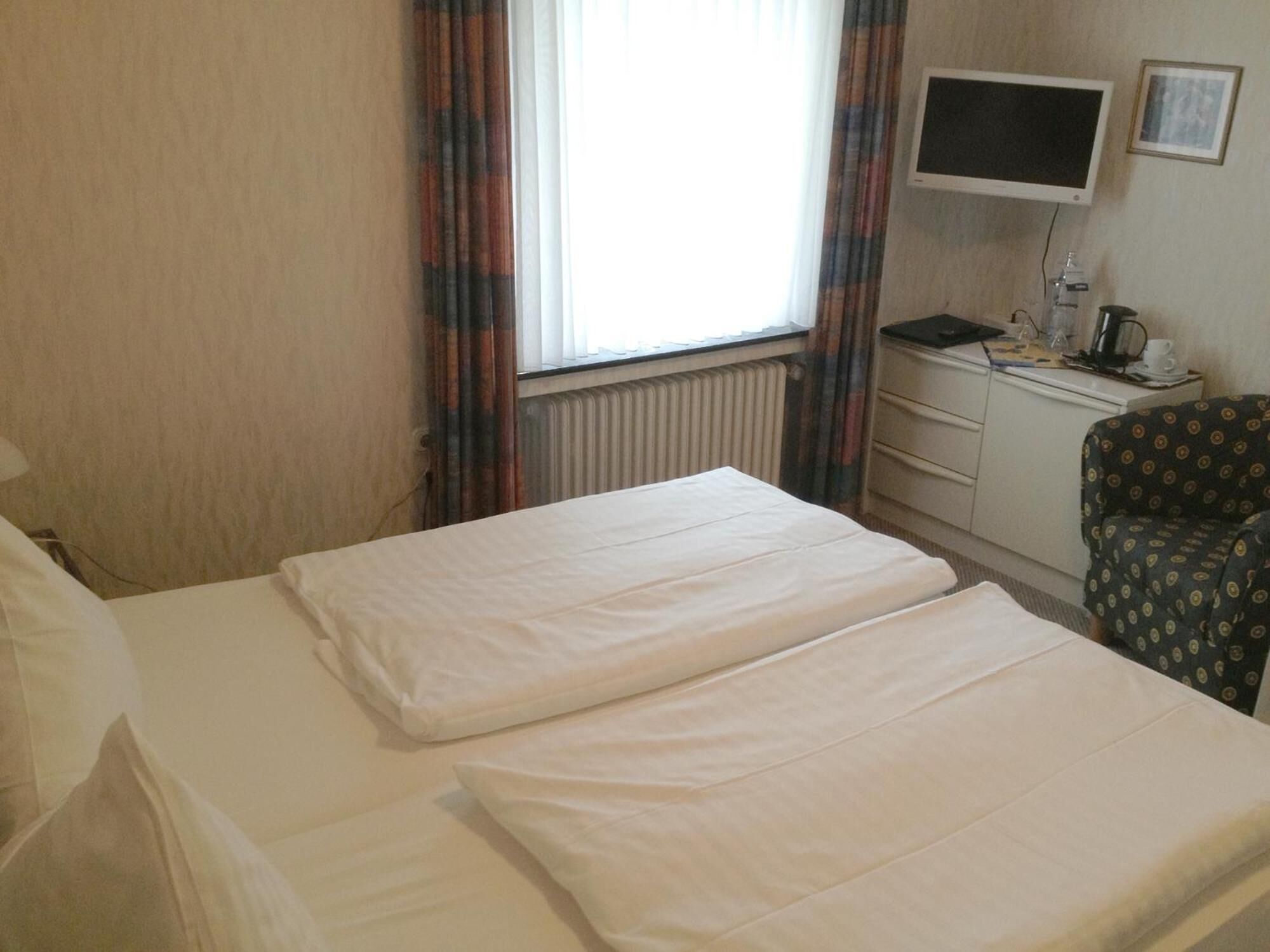 Una camera d'albergo con due letti, una scrivania con un computer, una sedia, un televisore e una finestra con tende.