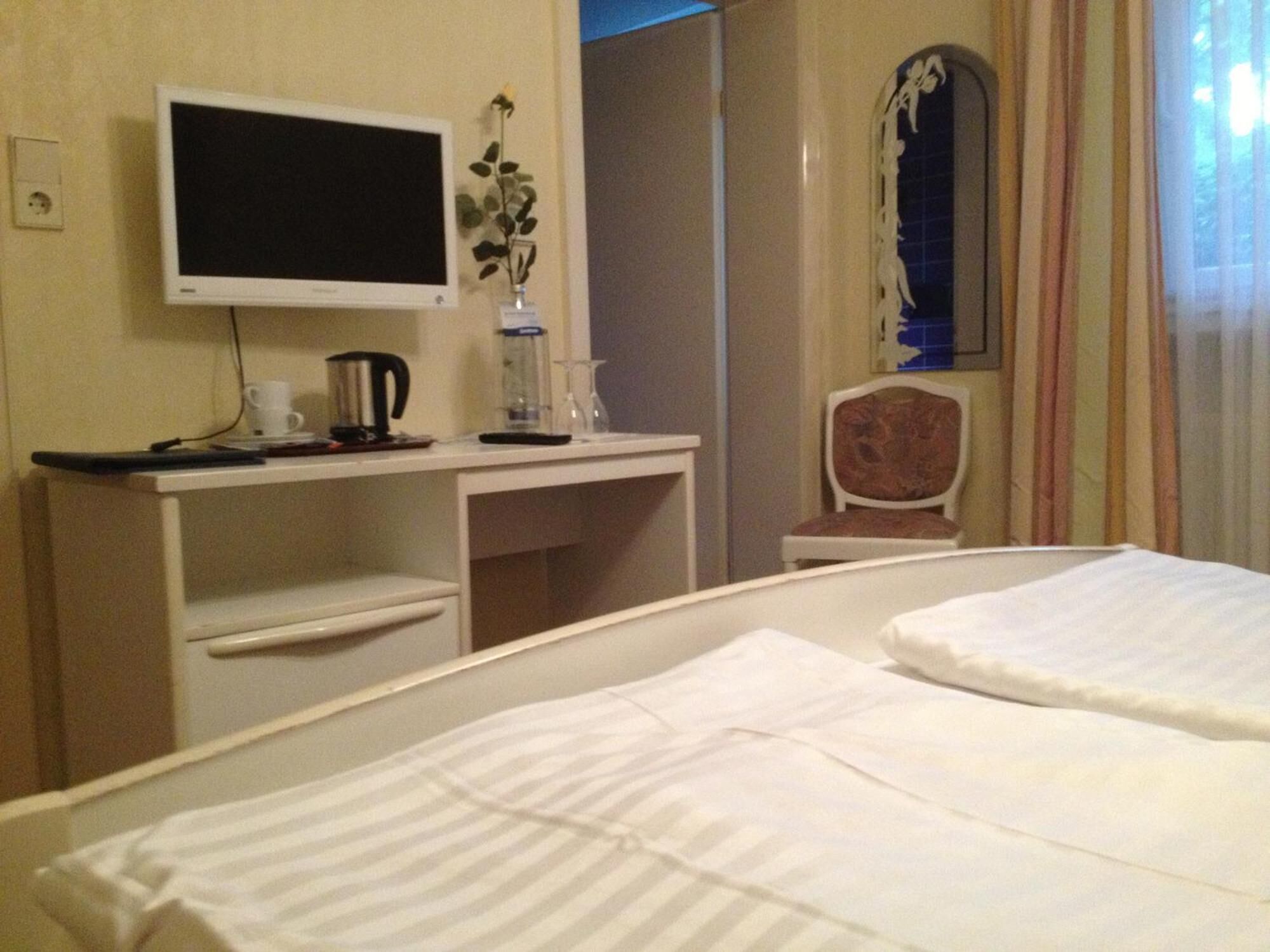 A hotel room with a bed, a desk, a chair, a TV, and a window with curtains.