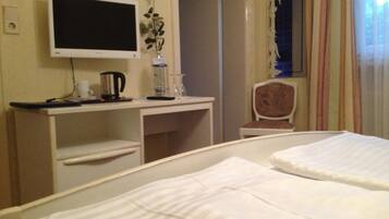 A hotel room with a bed, a desk, a chair, a TV, and a window with curtains.