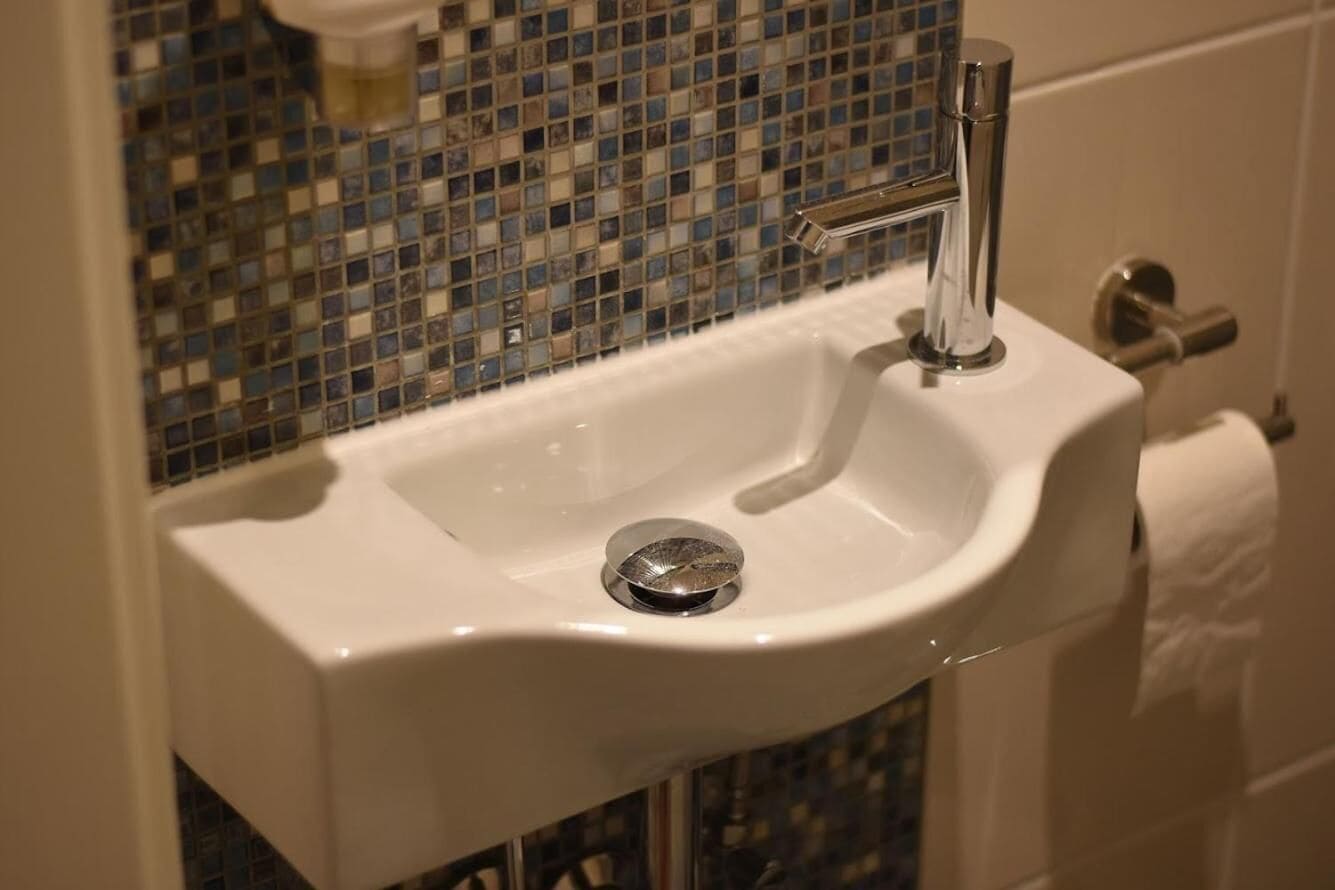 Un lavabo blanc pour la salle de bain, doté d’un robinet chromé, d’un drain et d’un pare-éclaboussures en mosaïque.