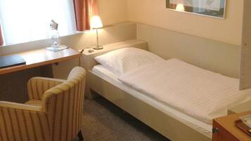 A hotel room with a single bed, a desk with a chair, a lamp, and a painting on the wall.