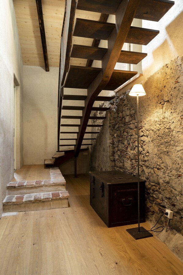 A wooden staircase leading to a stone wall, a floor lamp, and a small wooden chest.