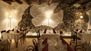 A dining area with stone walls and wooden beams, tables set with red napkins and candles.