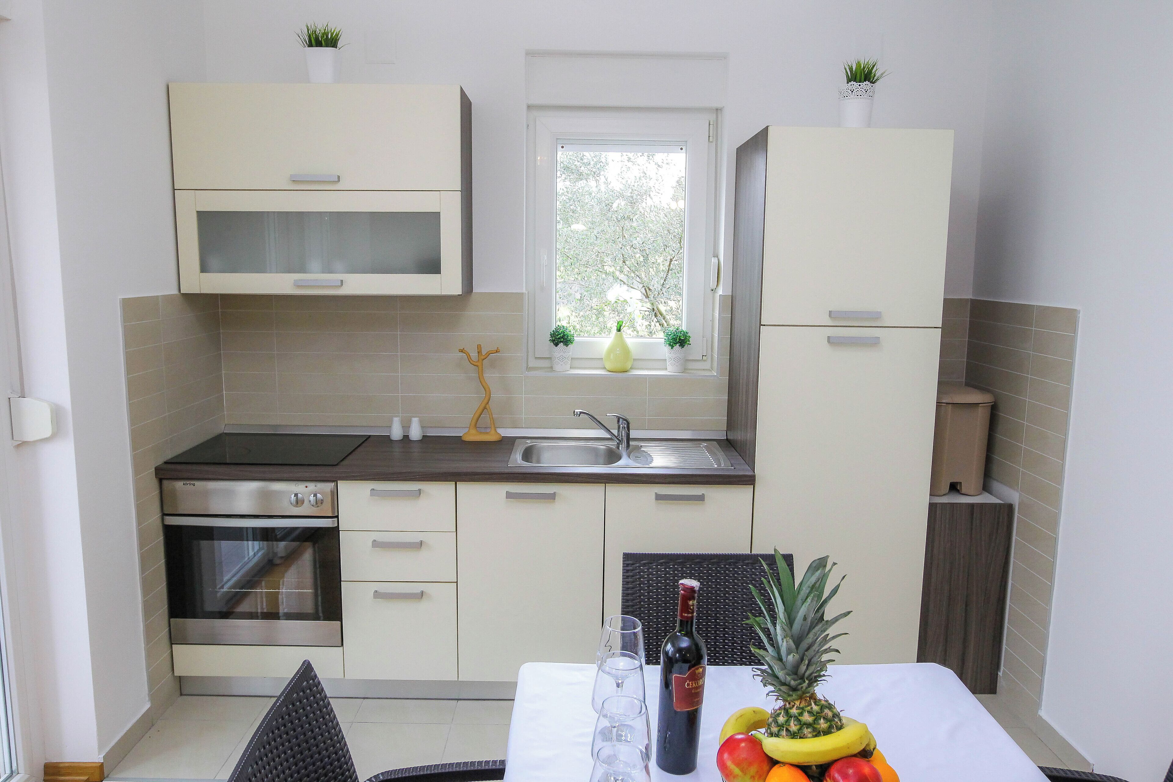 A compact kitchen with a built-in oven, a sink, and a window with potted plants.