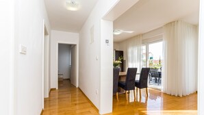 Una habitación amplia con suelo de madera, un comedor con sillas y un gran ventanal con cortinas.