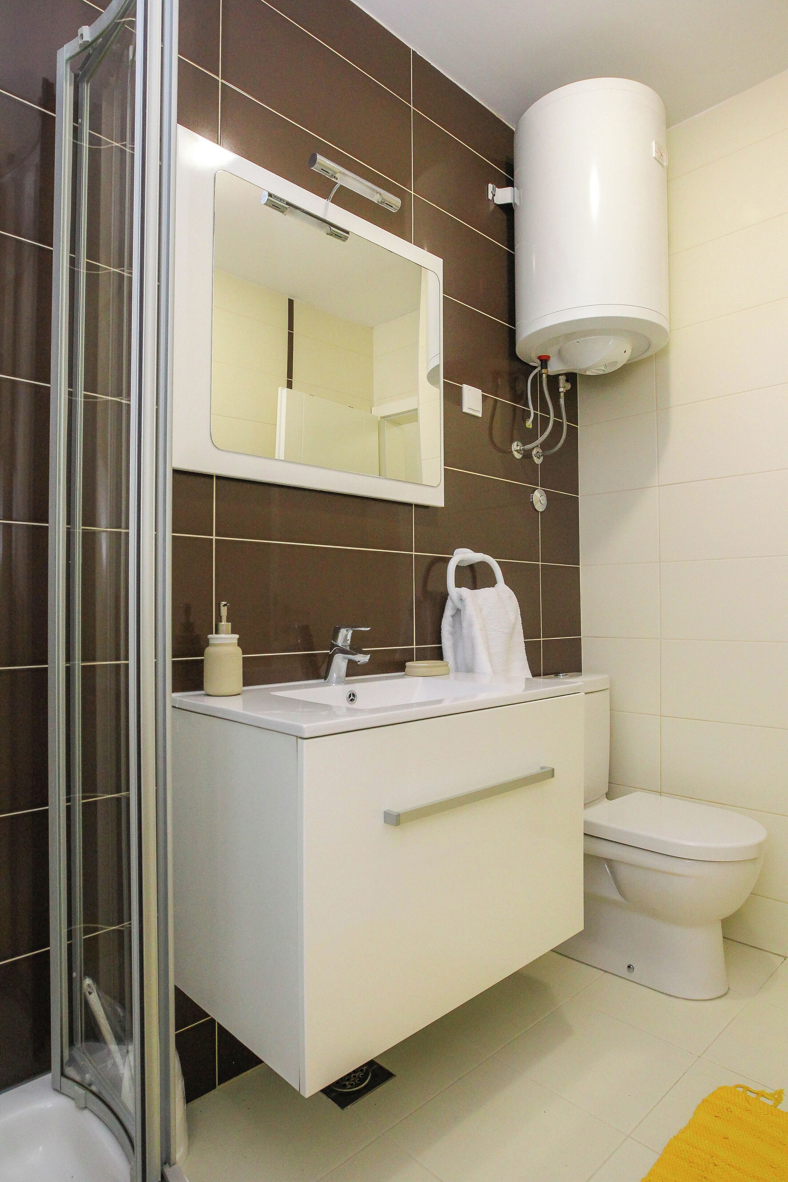Une salle de bain avec une douche à parois de verre, un lavabo blanc avec un miroir au-dessus et des toilettes.