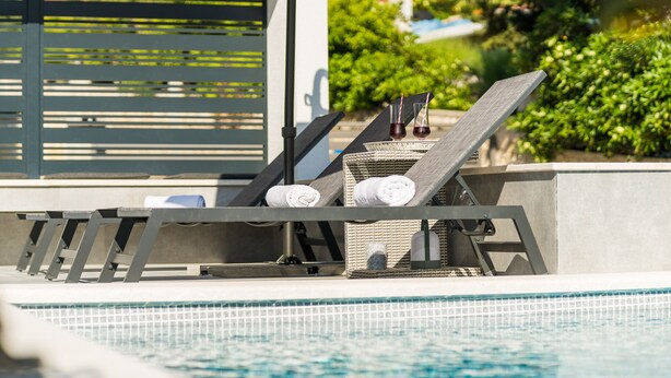Un área junto a la piscina con sillas de descanso, toallas y una cesta de mimbre.