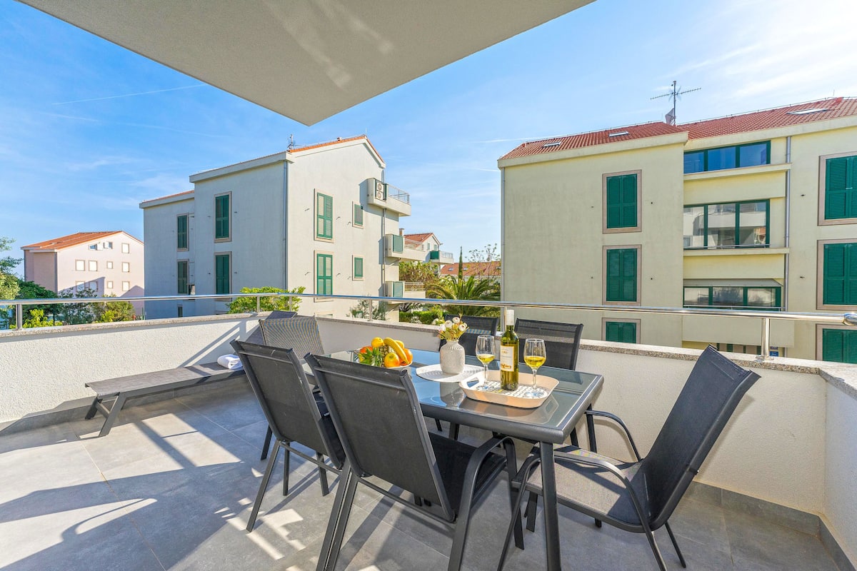 Un balcon avec une table dressée pour deux personnes, des chaises et une bouteille de vin.