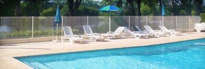 A swimming pool with white lounge chairs and a metal fence. - Camping les Bo-Bains (Badefols-sur-Dordogne)
