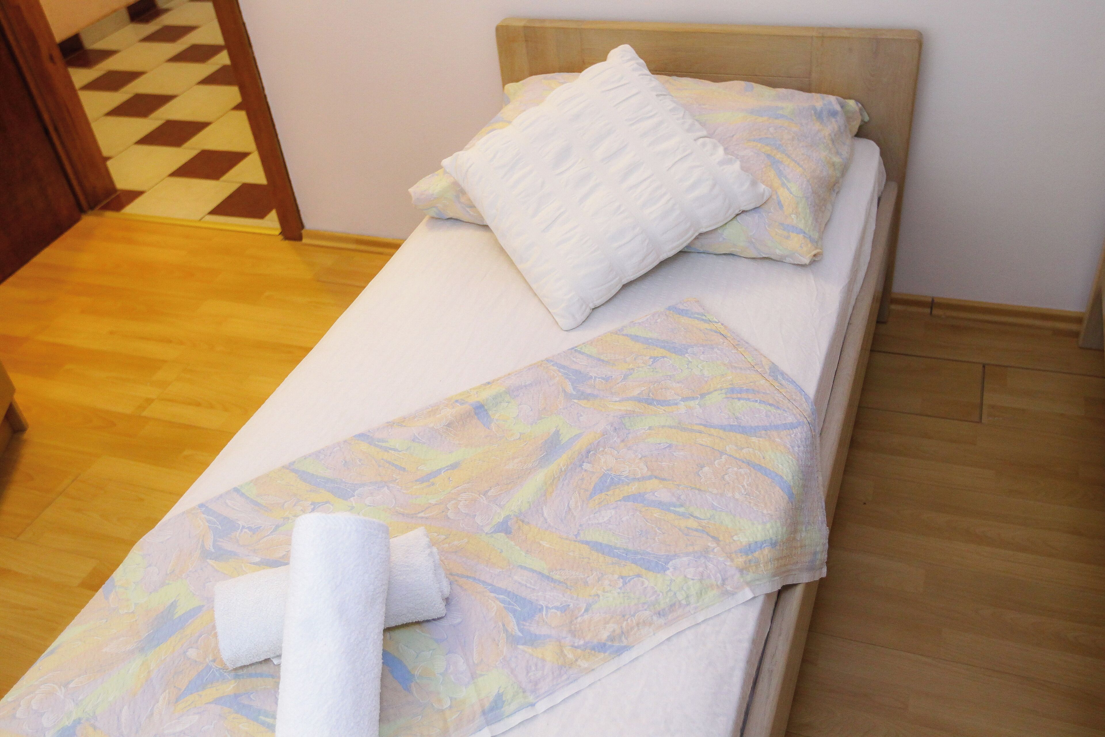 A single bed with a wooden headboard, a white pillow, and a floral-patterned bedspread.