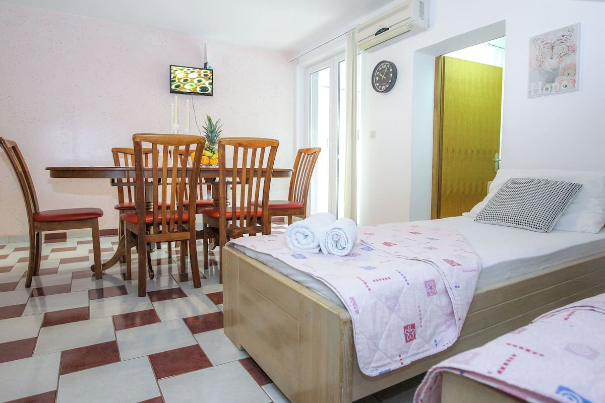 A room with a bed, a small table with chairs, a pineapple, and a TV on the wall.
