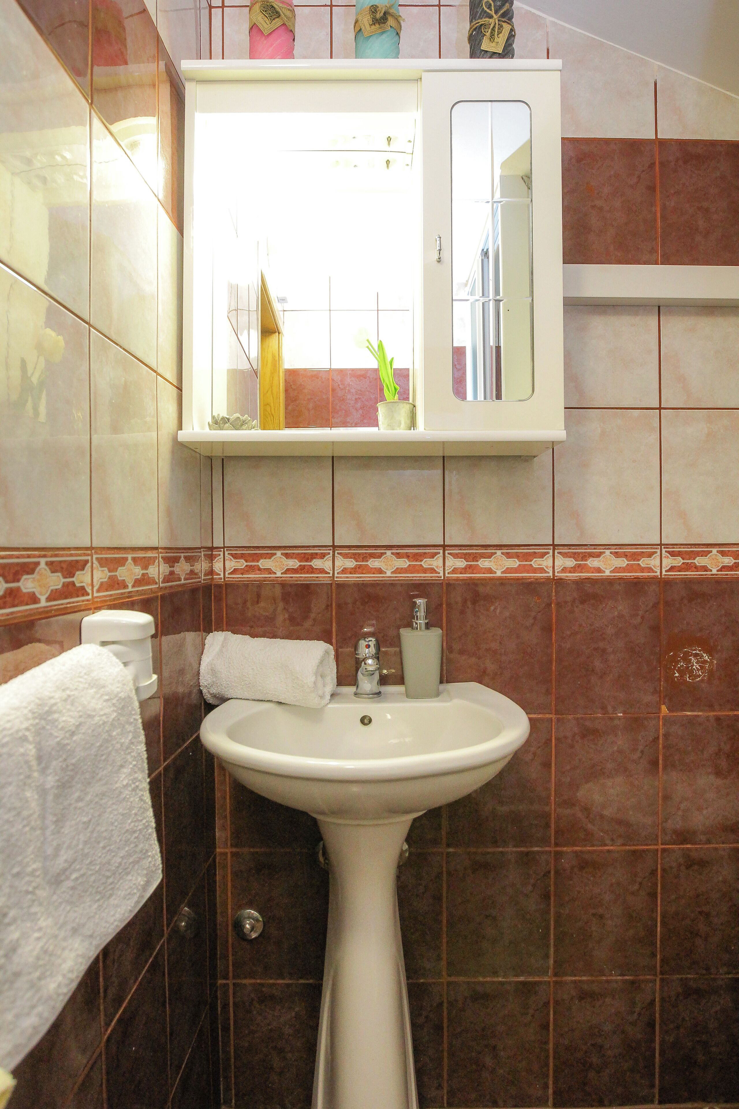 Un baño con lavamanos pedestal, un espejo encima y un perchero a la izquierda.