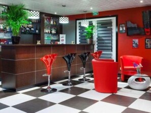 Eine Lobby mit Schachbrettmuster-Boden, einem Empfangsbereich und roten und schwarzen Barhocker.