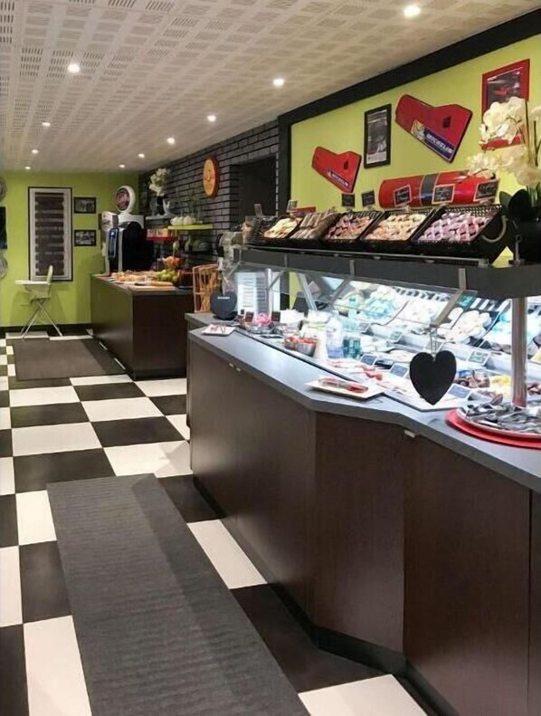 Un mostrador de charcutería con piso a cuadros, una vitrina de vidrio con alimentos y una pared con varios carteles y una decoración con forma de corazón.