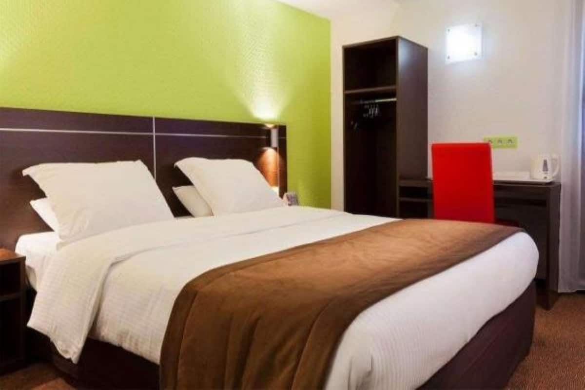 A hotel room with a bed, a wardrobe, and a desk with a red chair.