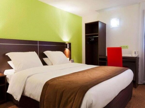 Habitación de hotel con una cama, un armario y un escritorio con una silla roja.