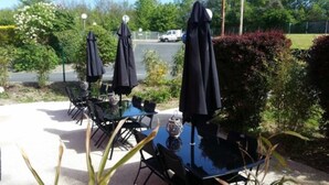 Buiten tafels en stoelen met parasols, een microfoon en een parkeerplaats op de achtergrond.