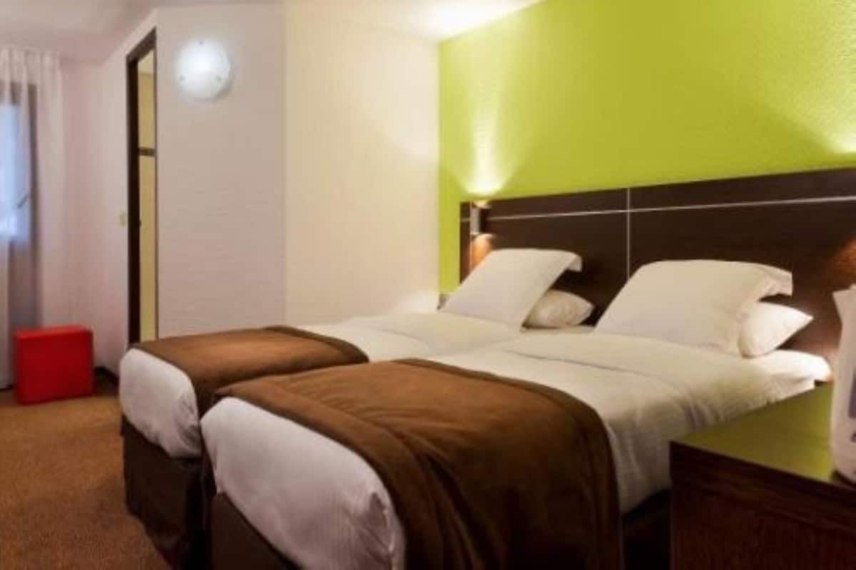 A hotel room with two beds, a green accent wall, a red stool, and a nightstand with a lamp.