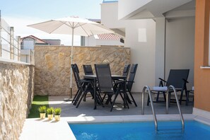A poolside area with a stone wall, a table with chairs, and a pool with a ladder. - Funtastic Apartment with Private Heated Pool (Novalja)