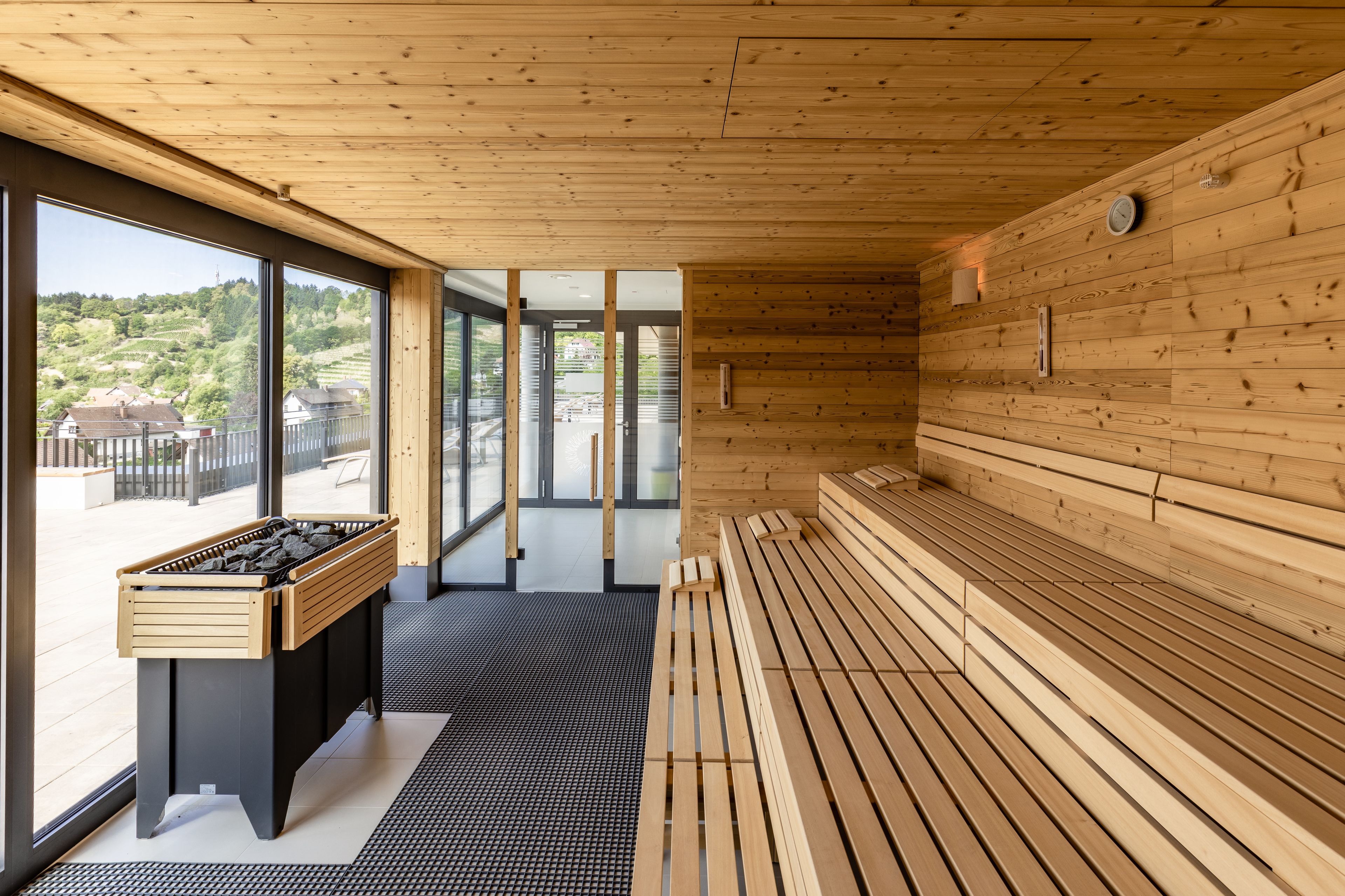 Ein Saunaraum mit Holzbänken und einem Holztisch, große Fenster mit Blick ins Freie.