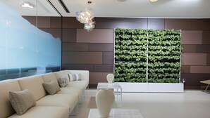 A modern waiting area with a sofa, a vase, a glass table, and a green vertical garden wall. - Sonnenhof Hotel & Restaurant (Lautenbach)