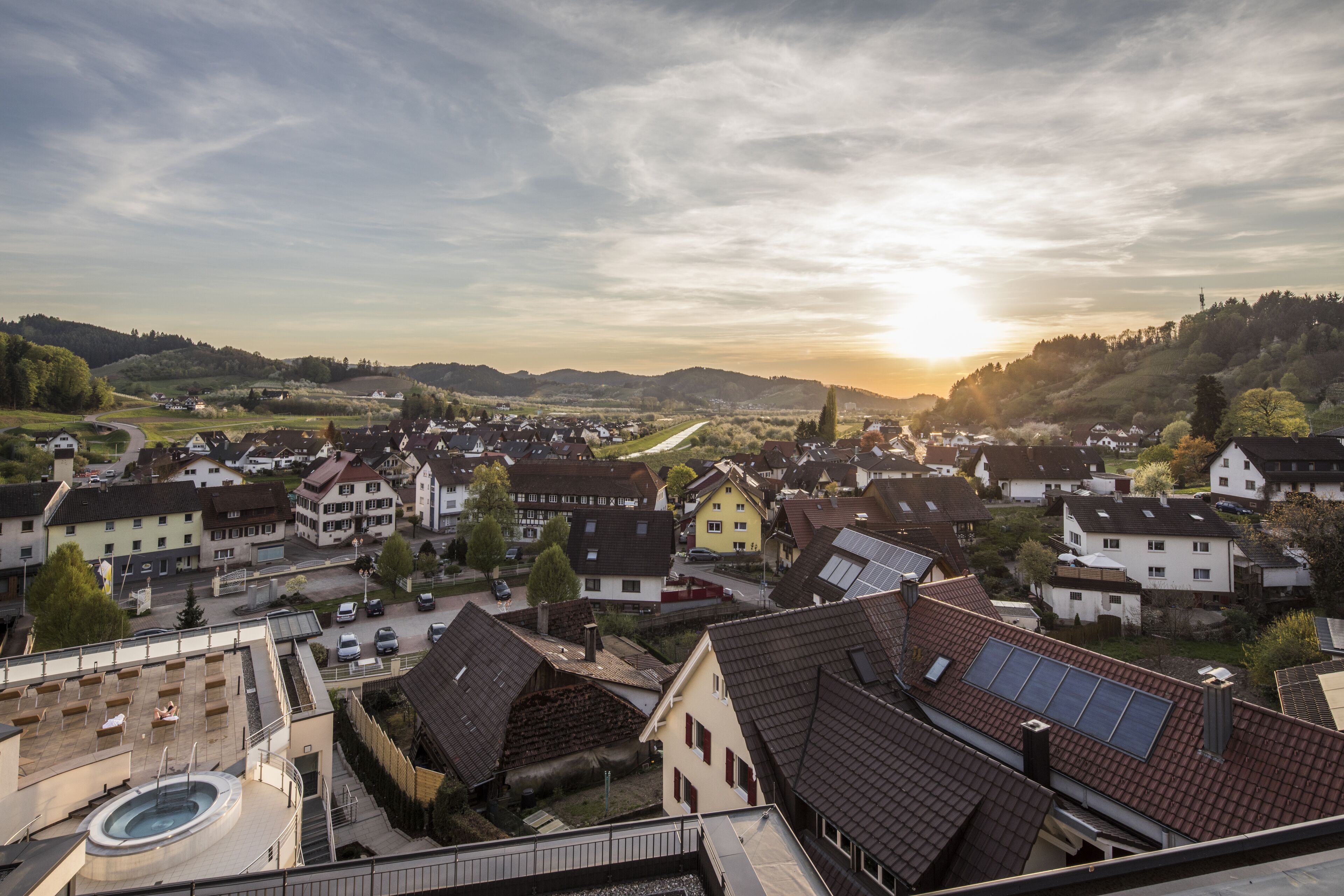 A residential area with houses, a swimming pool, and a hilly landscape in the background.