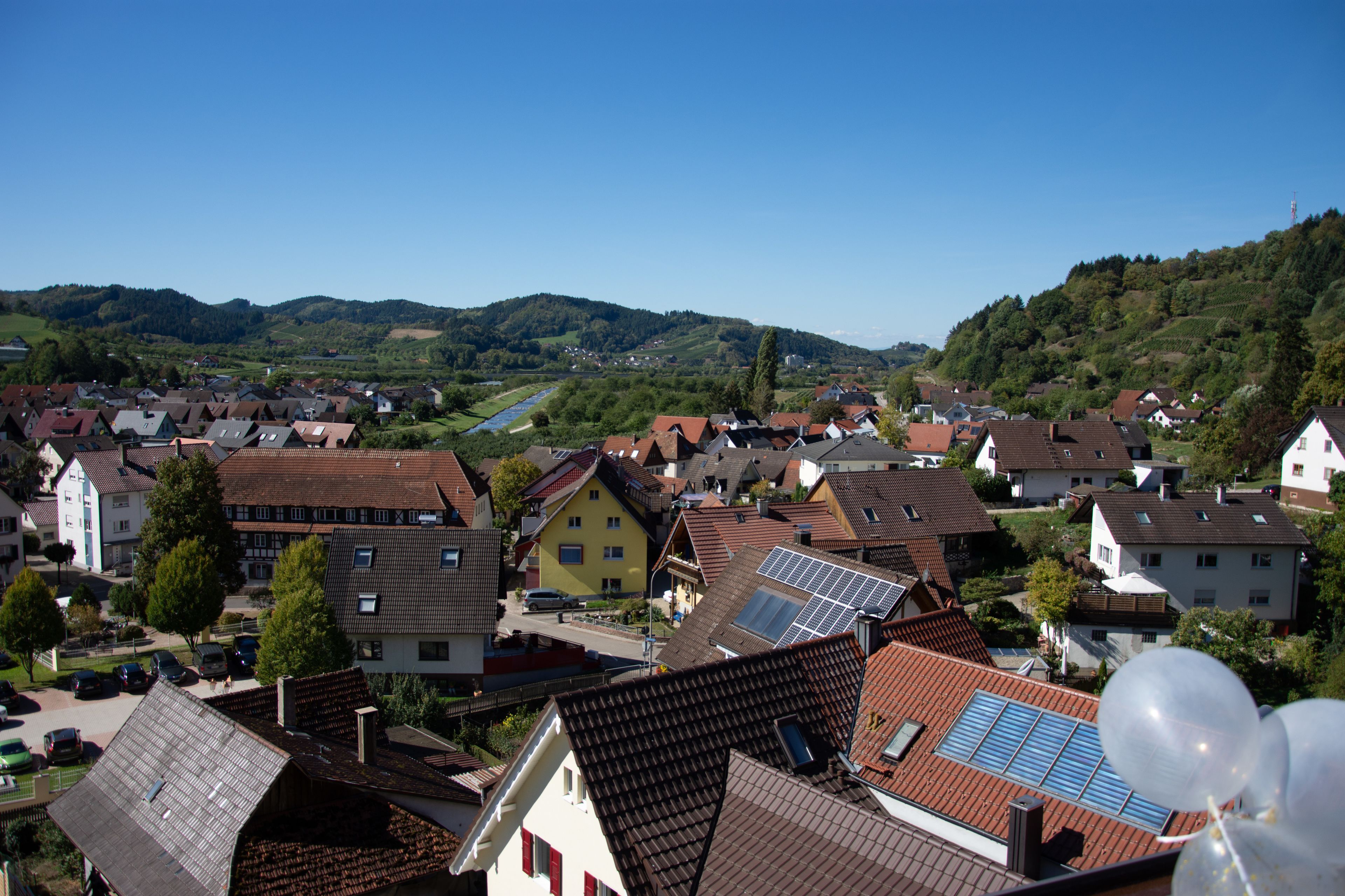A residential area with houses, some with solar panels, and a river in the background.