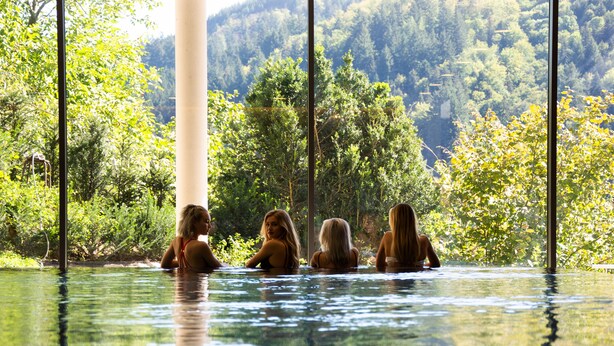 A pool with four people sitting at the edge, surrounded by lush greenery and a forested hillside. - Sonnenhof Hotel & Restaurant (Lautenbach)