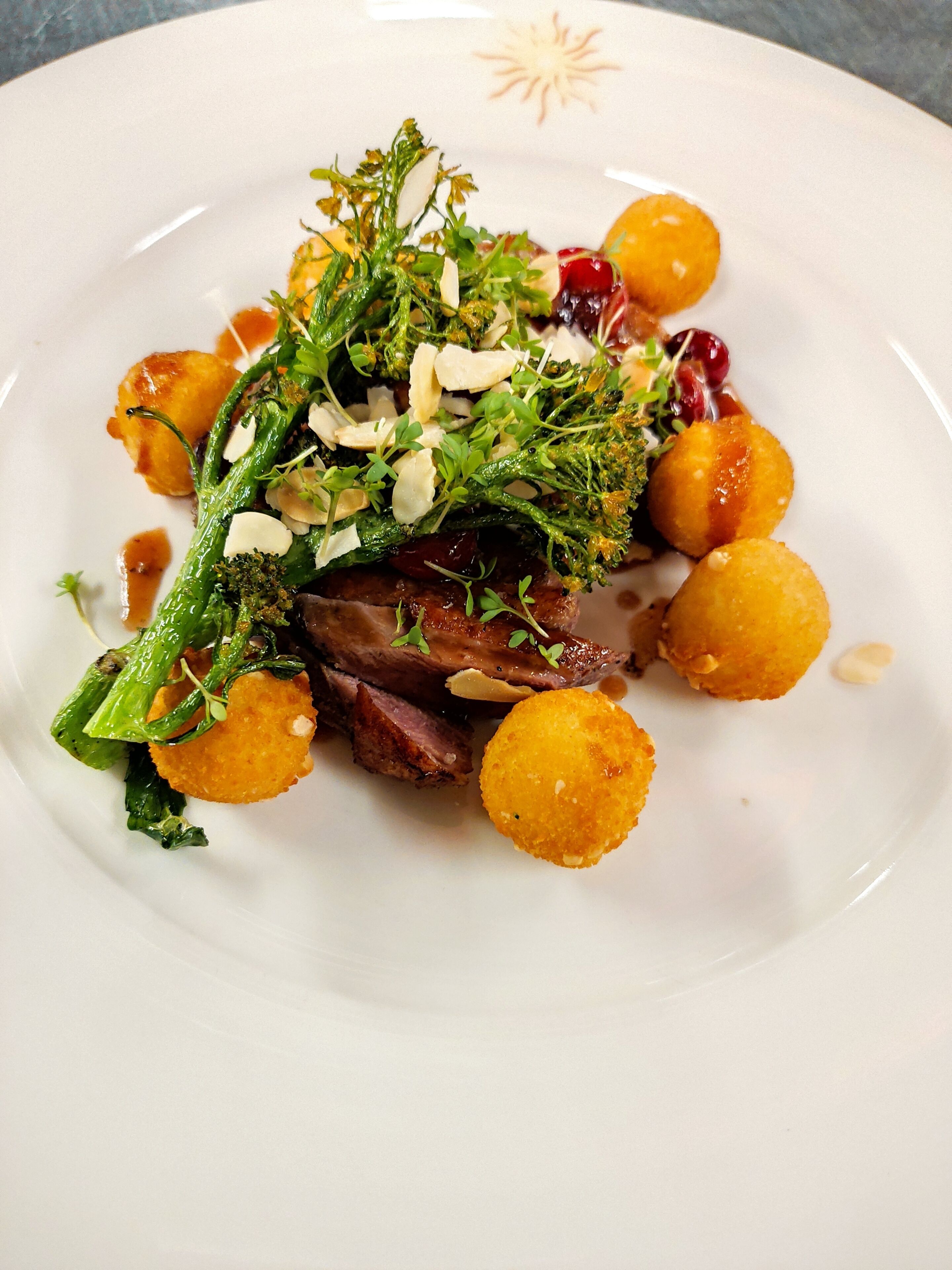Une assiette blanche contenant un plat composé de viande, de légumes verts et de petites portions de légumes ronds, peut-être des pommes de terre, le tout agrémenté d’herbes.
