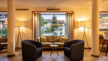 Una habitación de hotel moderna con sofá, dos sillones, una mesita redonda y lámparas de pie.