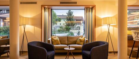 A modern hotel room with a sofa, two armchairs, a small round table, and floor lamps.
