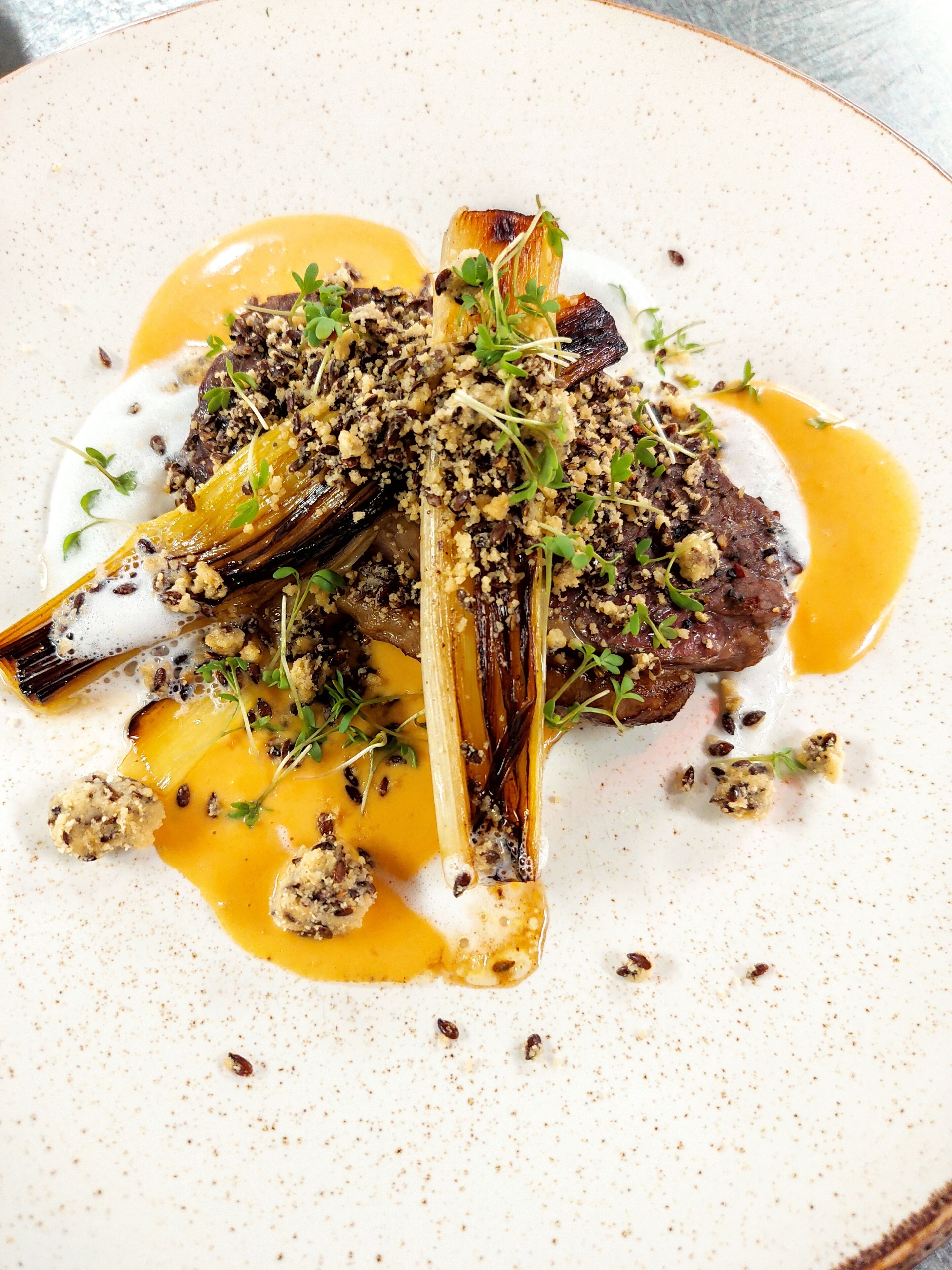A plate of food with a lamb shank, vegetables, and a creamy sauce.