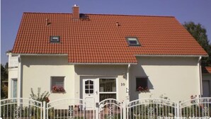 Een huis met twee verdiepingen, voorzien van een rode dakbedekking, een witte gevel en een klein balkon met bloemen.