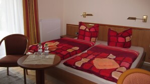 Een hotelkamer met twee bedden, een houten hoofdbord, een klein rond tafeltje met een fles en een glas, en een stoel.