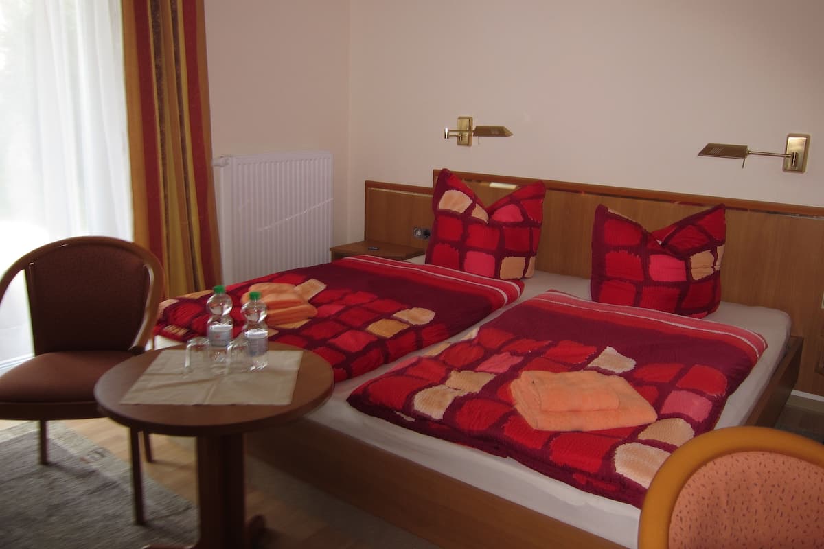 Habitación de hotel con dos camas, cabecera de madera, una mesita redonda con una botella y un vaso, y una silla.