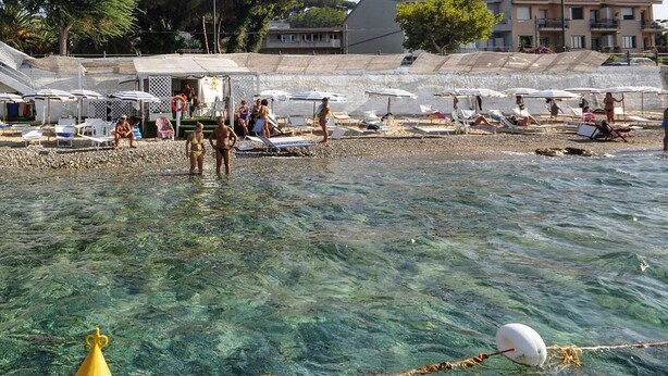 A beach with clear water, umbrellas, and people. - Il Ritrovo di Ulisse Bed & Breakfast (Villa San Giovanni)