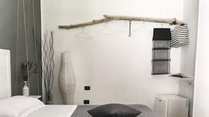 A bedroom with a bed, a bedside table, a radiator, and a wall-mounted shelf with a lamp and a hanging garment rack. - Il Ritrovo di Ulisse Bed & Breakfast (Villa San Giovanni)