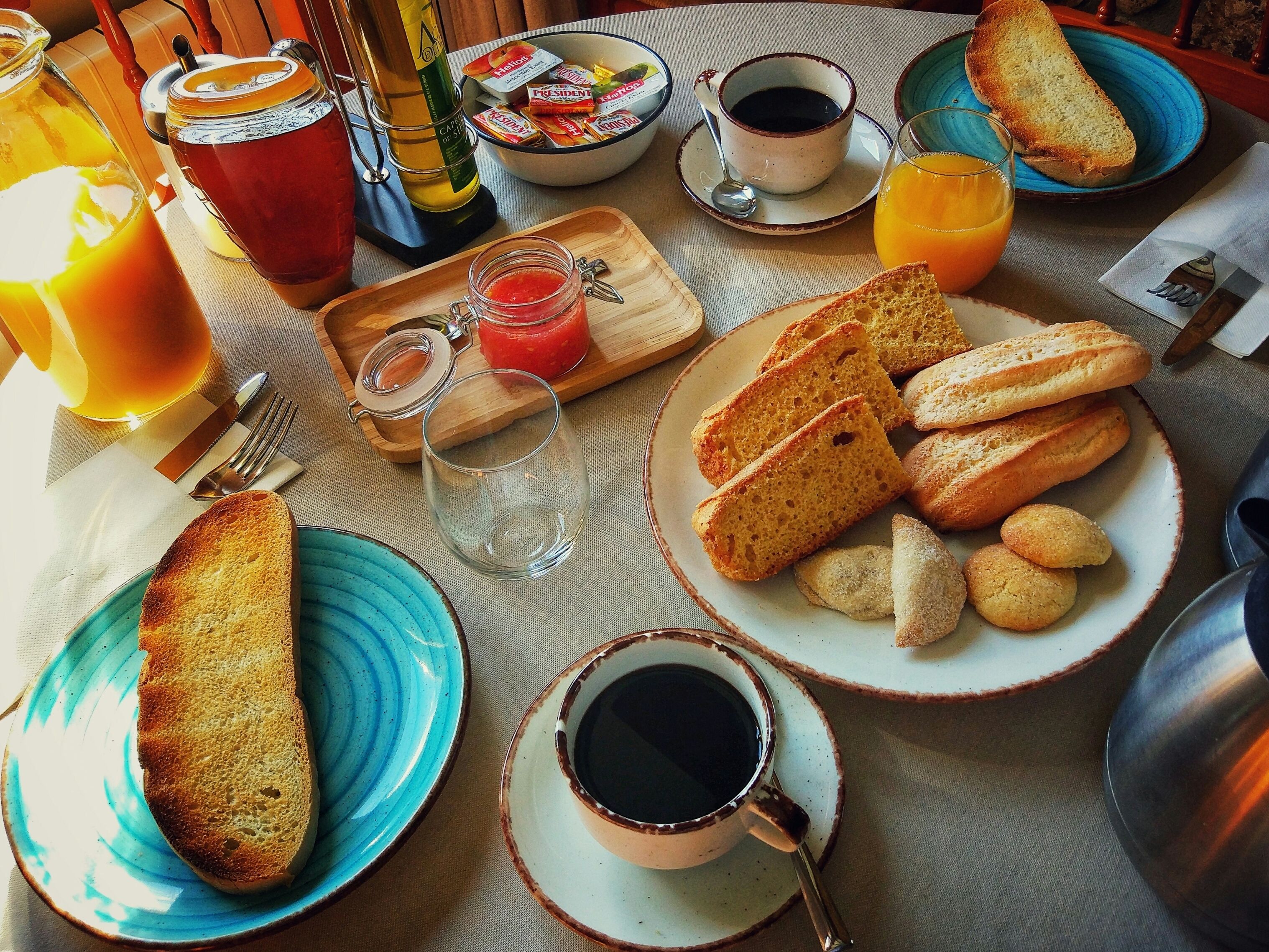 A breakfast table with toast, pastries, coffee, juice, and condiments.