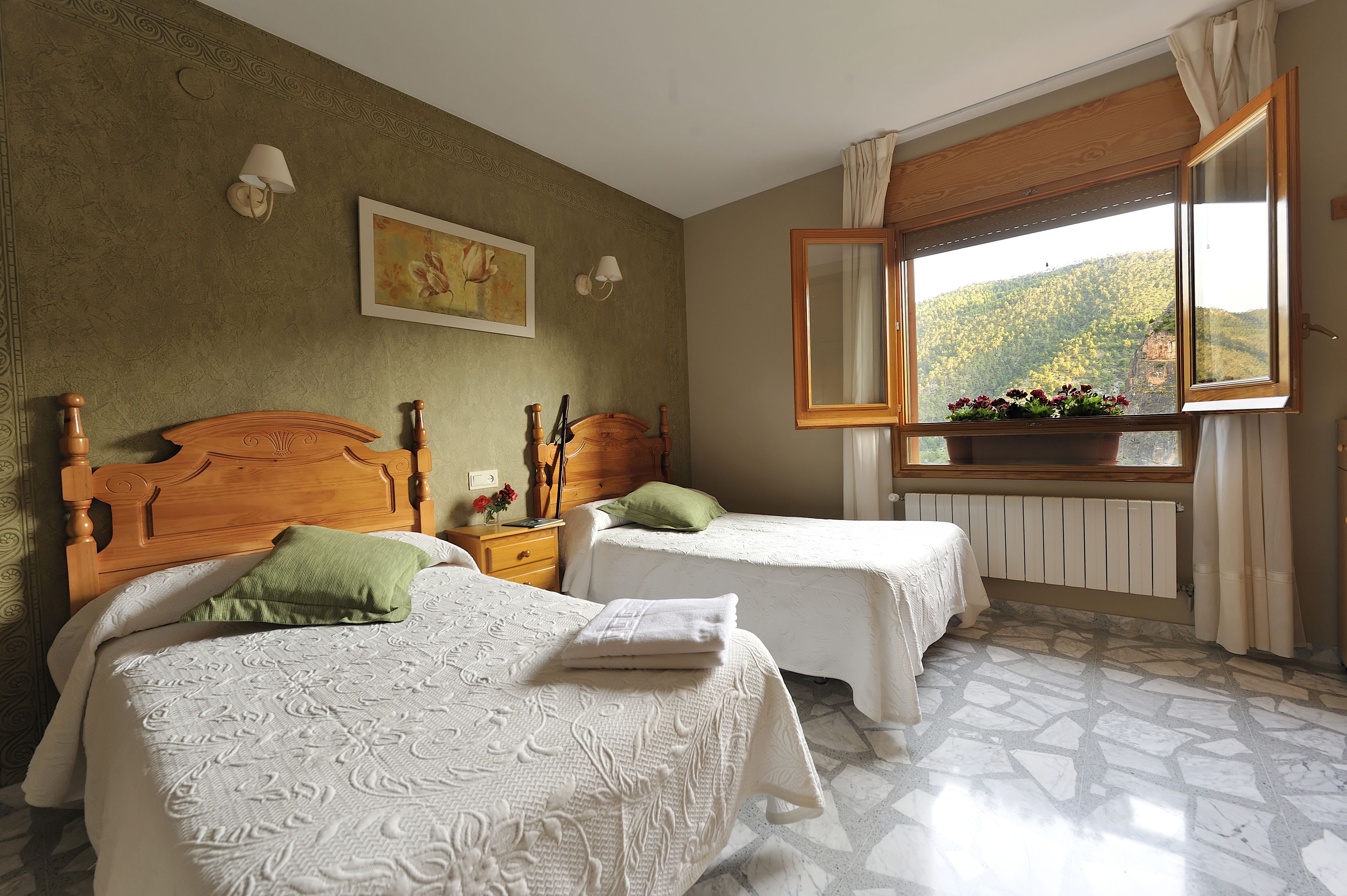 Una stanza con due letti, una testiera in legno, un comodino, una finestra con vista su una montagna e un quadro appeso al muro.