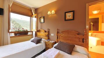 A hotel room with two single beds, a wooden headboard, a nightstand, a bedside table, a window with curtains, a wall-mounted lamp, and a framed picture.