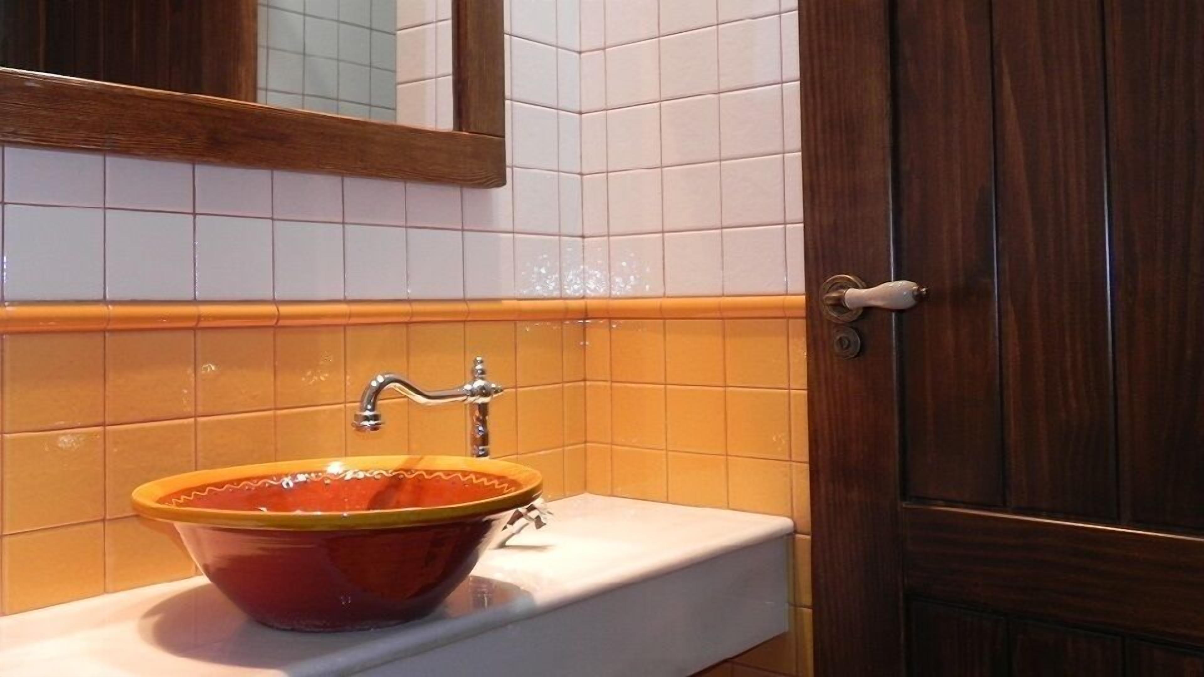 Un baño con un lavamanos de cerámica rojo, azulejos blancos y una puerta de madera.
