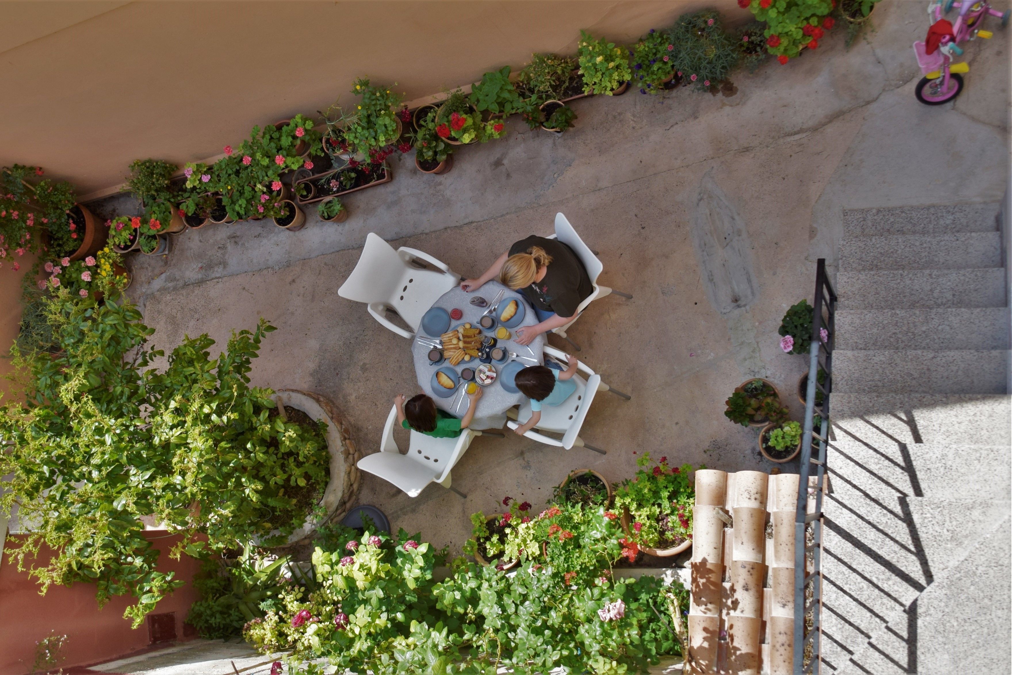 An outdoor patio with a round table and chairs, surrounded by potted plants and a staircase.