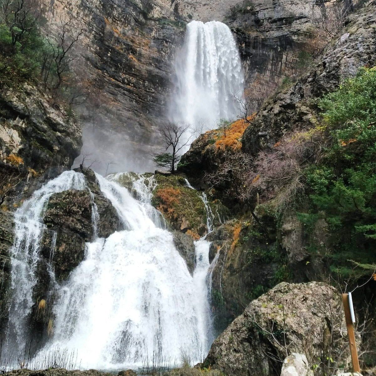 Een waterval stort neer over een rotsachtige klif, omringd door schaarse begroeiing.