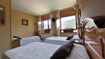 Habitación de hotel con dos camas, cabecero de madera, ventana con vistas a las colinas y un cuadro enmarcado en la pared.