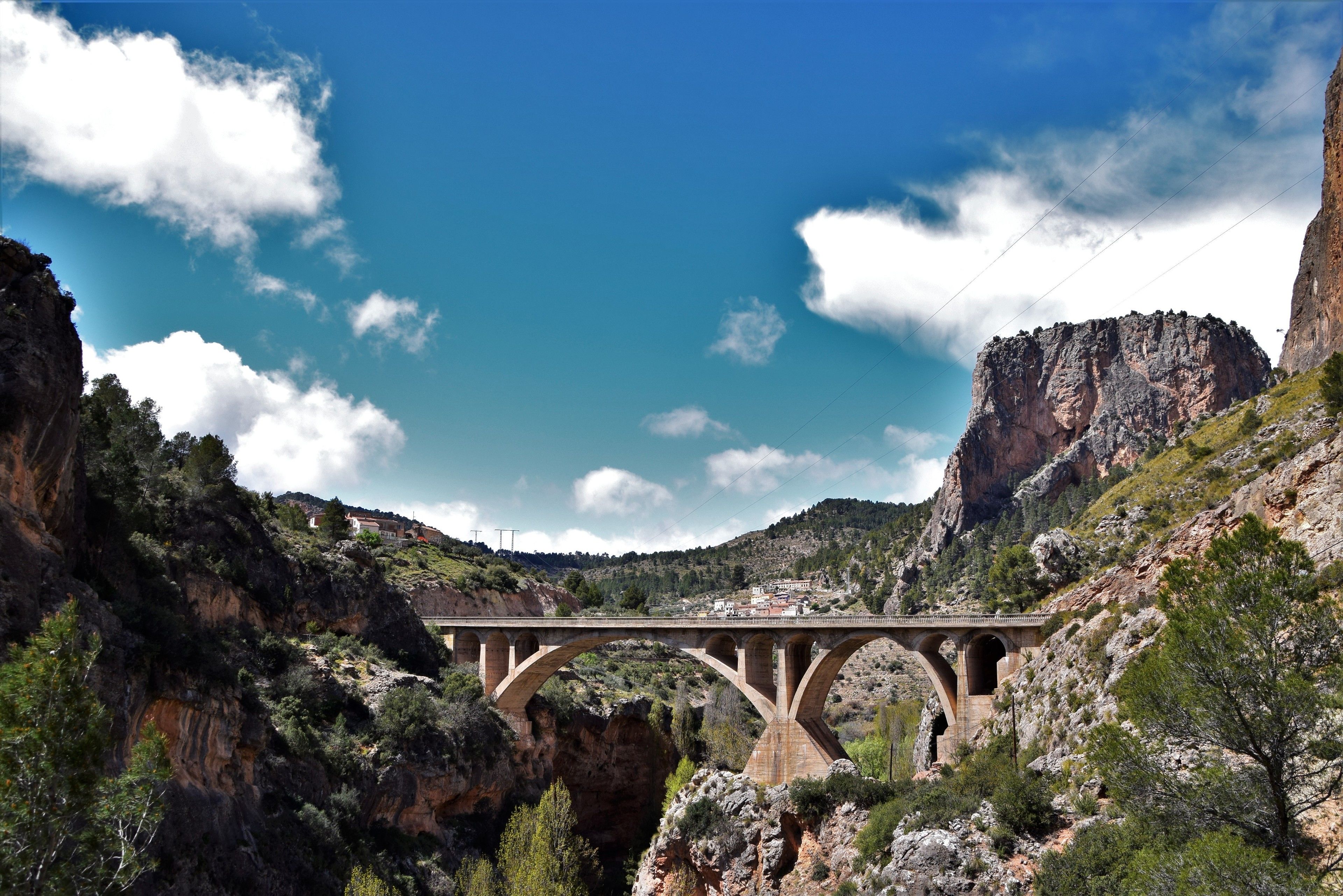 A stone bridge over a canyon with rocky terrain and sparse vegetation.