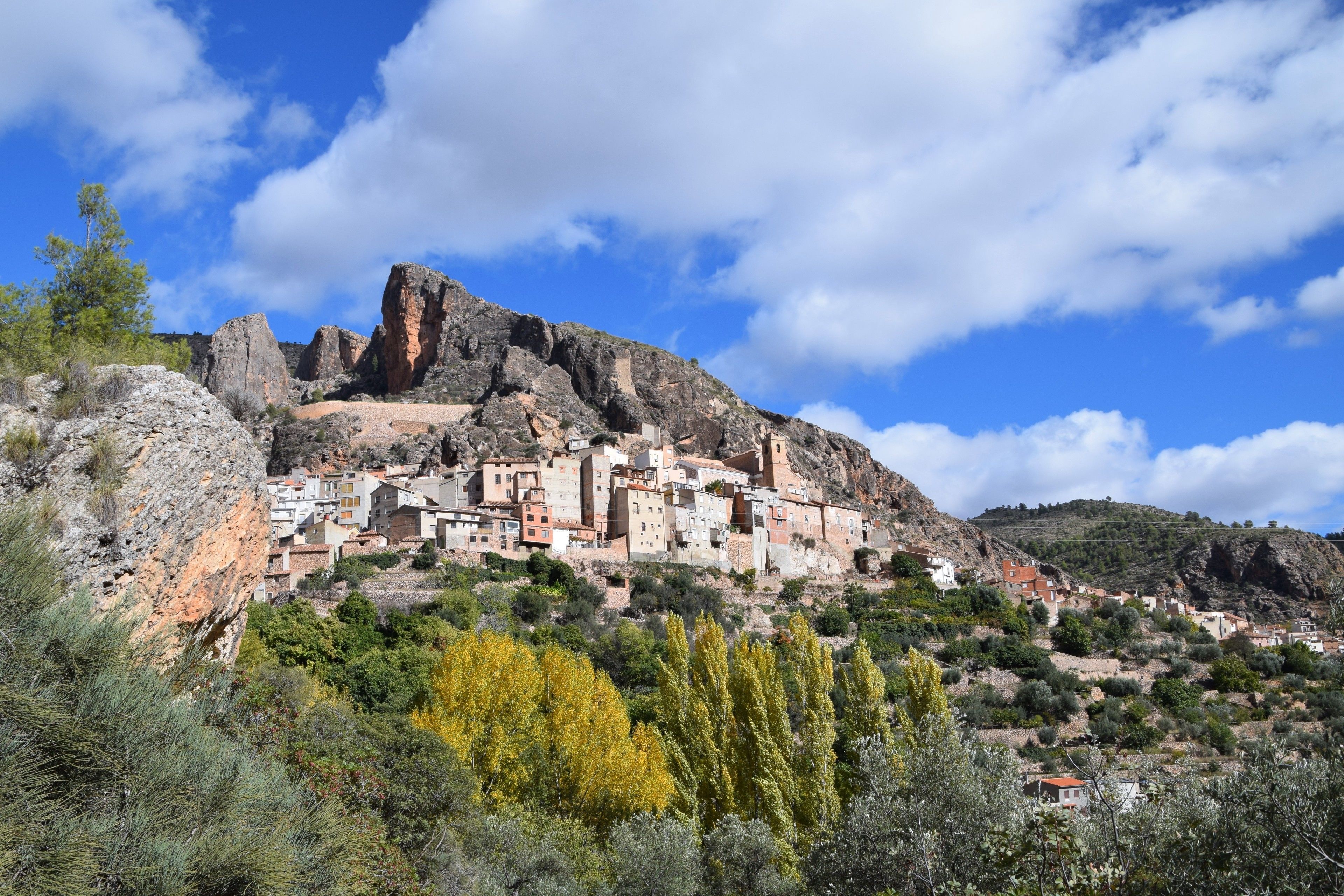 Un pueblo costero con edificaciones integradas en la ladera, con estructuras escalonadas y un imponente pico rocoso al fondo.